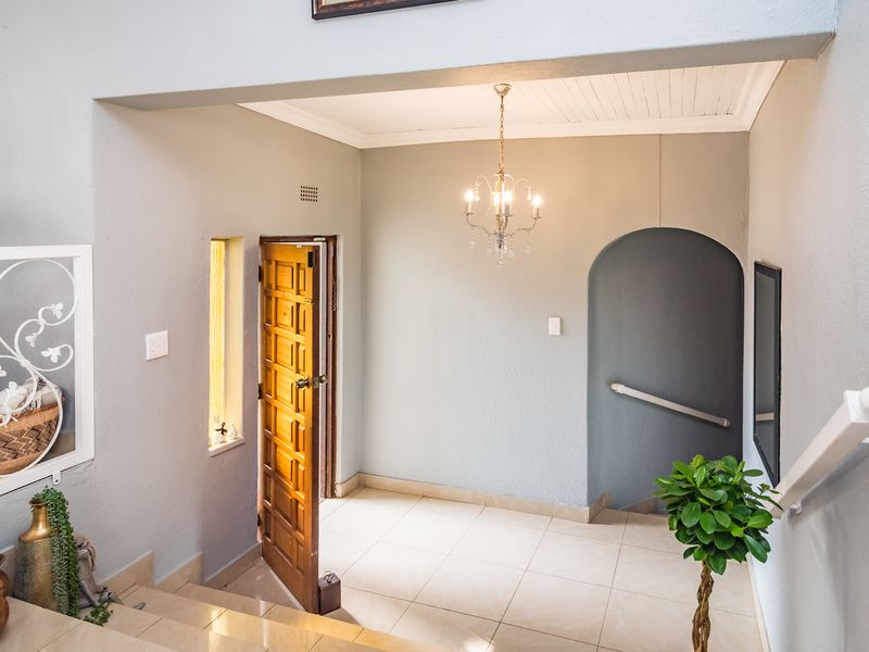 Welcoming entrance hall featuring tiled flooring, a classic timber front door, an elegant chandelier, and an arched transition to the staircase.