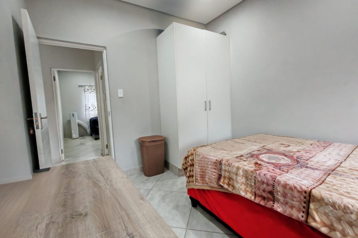 A bedroom featuring tiled flooring, a built-in wardrobe, and recessed ceiling lighting, with an adjacent hallway visible.