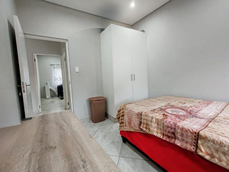 A bedroom featuring tiled flooring, a built-in wardrobe, and recessed ceiling lighting, with an adjacent hallway visible.