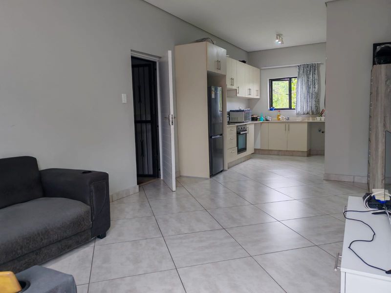 Open-plan living area featuring tiled flooring and a functional kitchen with built-in cabinetry, integrated oven, and hob.