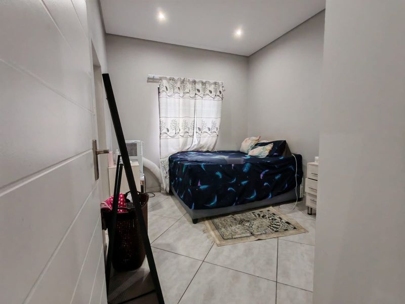 A functional bedroom featuring neutral wall tones, tiled flooring, and recessed ceiling lighting, providing a clean and simple living space.