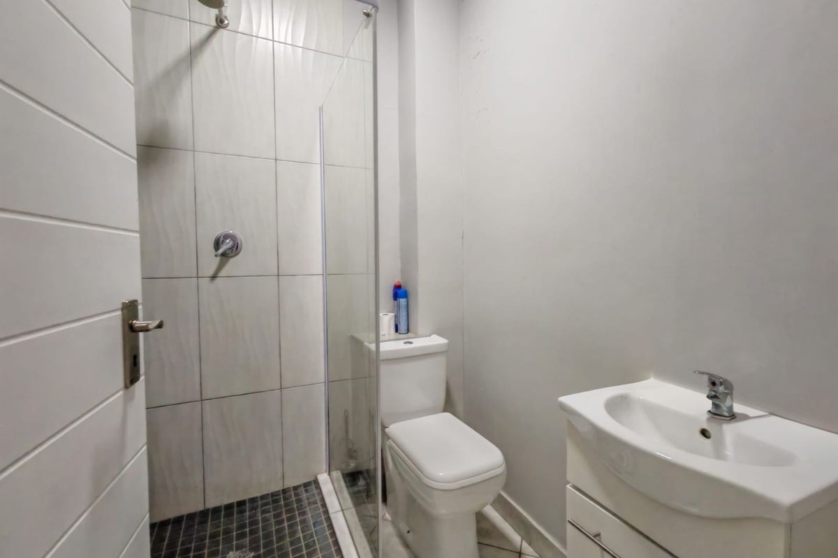A compact, modern bathroom featuring a glass-enclosed shower with textured wall tiles, a white vanity basin, and a standard toilet.