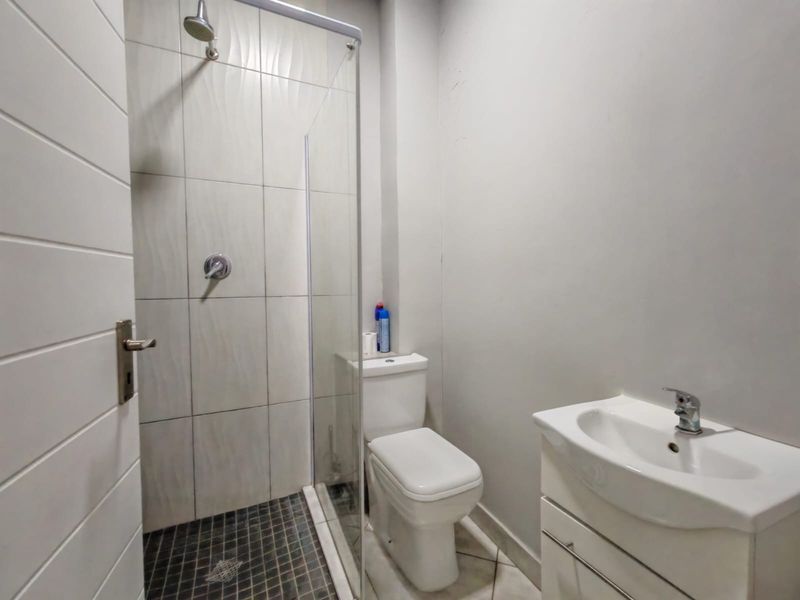 A compact, modern bathroom featuring a glass-enclosed shower with textured wall tiles, a white vanity basin, and a standard toilet.