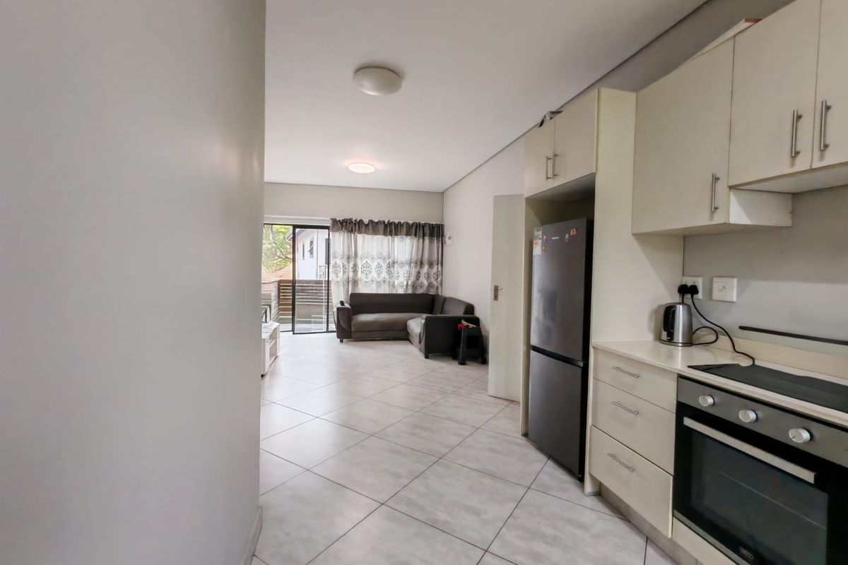 Open-plan living area featuring a functional kitchen with built-in cabinetry and appliances, flowing into a lounge space with access to an outdoor balcony.