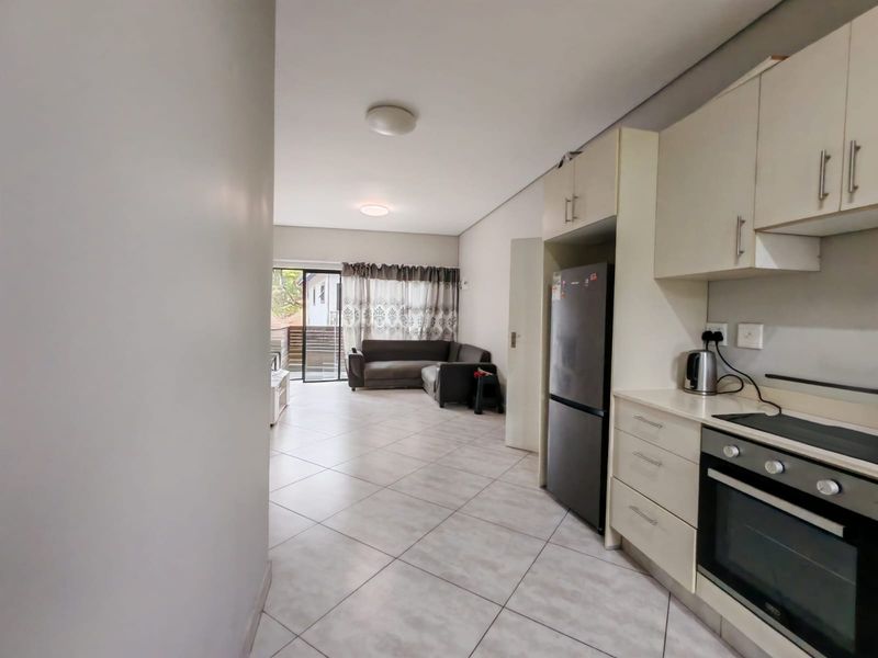 Open-plan living area featuring a functional kitchen with built-in cabinetry and appliances, flowing into a lounge space with access to an outdoor balcony.