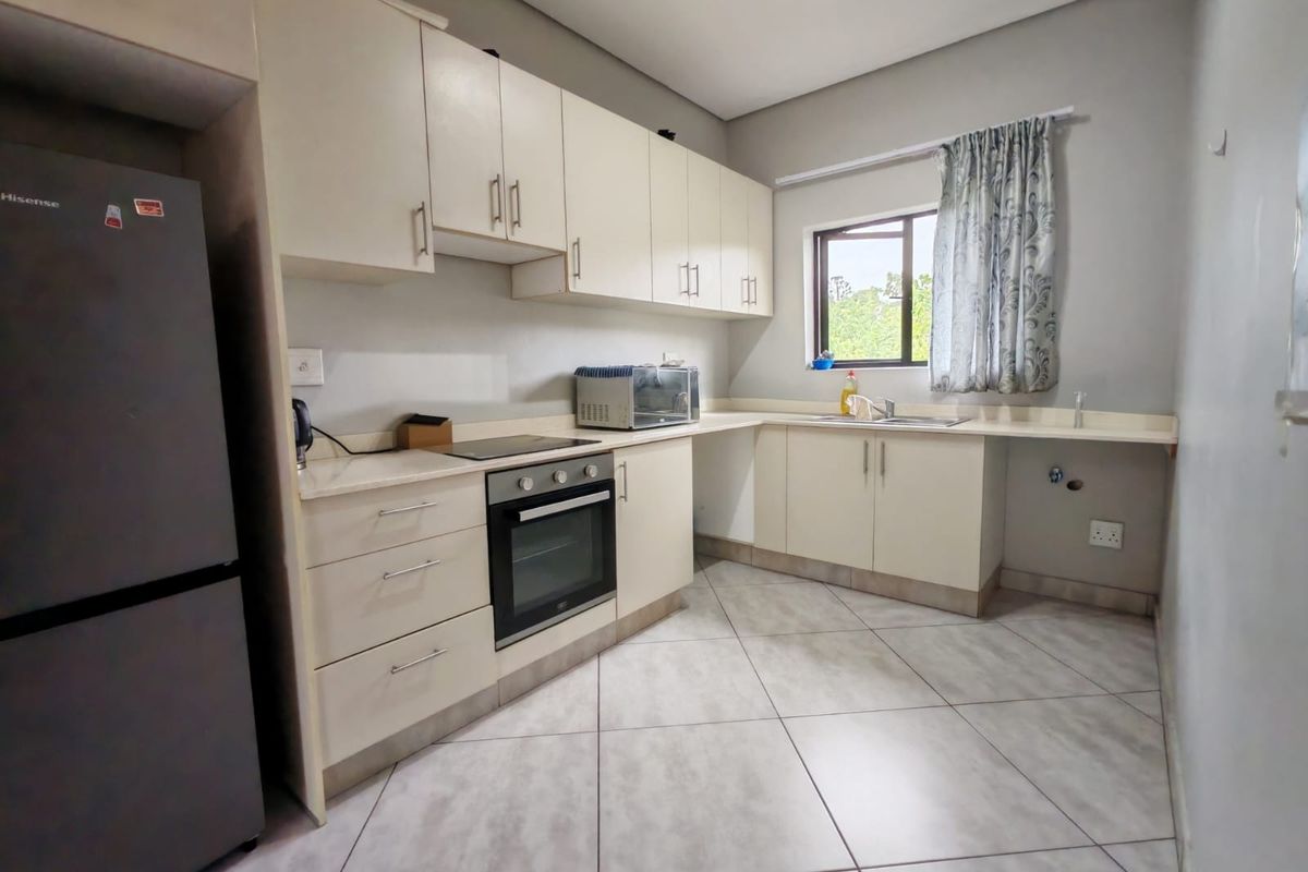 A functional kitchen featuring light-toned cabinetry, laminate countertops, built-in oven, electric hob, and tiled flooring with space for under-counter appliances.