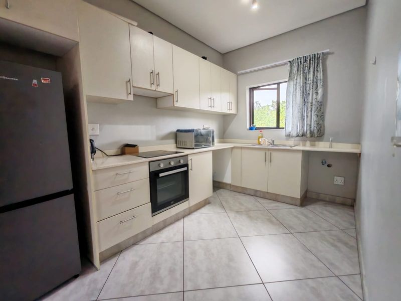 A functional kitchen featuring light-toned cabinetry, laminate countertops, built-in oven, electric hob, and tiled flooring with space for under-counter appliances.