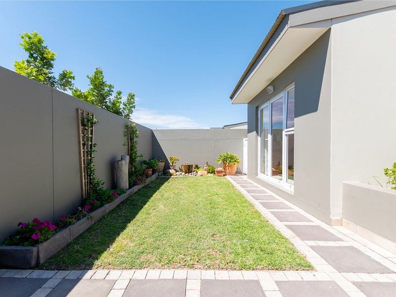 A well-maintained rear garden featuring a neat lawn, paved walkway, and high boundary walls, providing a private and tidy outdoor space.