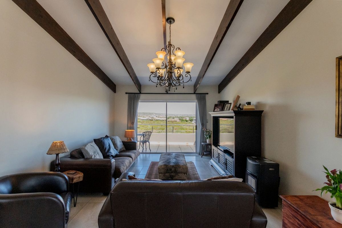 Spacious living room featuring exposed timber ceiling beams, tiled flooring, and large sliding glass doors that open to a scenic outdoor balcony.