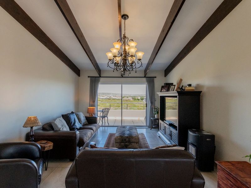 Spacious living room featuring exposed timber ceiling beams, tiled flooring, and large sliding glass doors that open to a scenic outdoor balcony.
