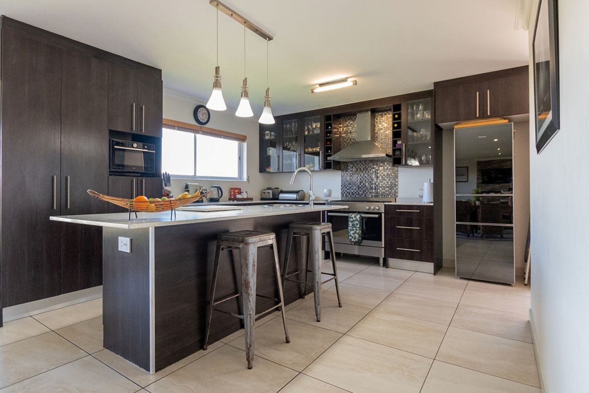Modern kitchen featuring dark wood cabinetry, a central island with stone countertops, stainless steel appliances, and a decorative mosaic tile backsplash.