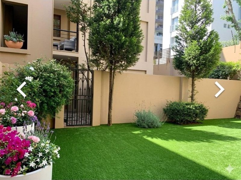 A well-maintained private garden featuring artificial turf, established trees, and a secure wrought iron gate, providing a neat outdoor space.