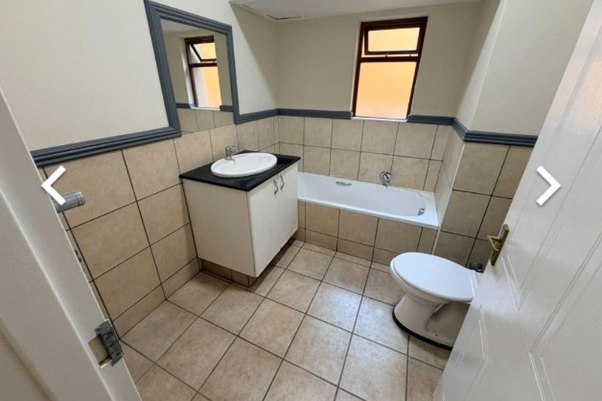 A functional bathroom featuring a built-in vanity with a basin, a standard bathtub, and a toilet, finished with neutral wall and floor tiling.