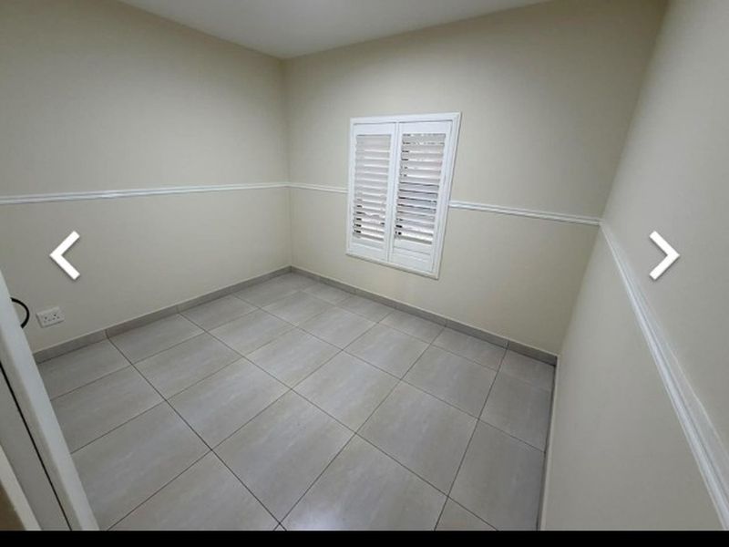 A clean, empty bedroom featuring neutral tiled flooring, chair rail molding, and white plantation shutters, offering a versatile space ready for personalization.