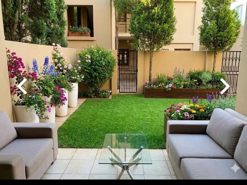 A well-maintained private patio area featuring tiled flooring, a manicured lawn, and established garden beds enclosed by a boundary wall.