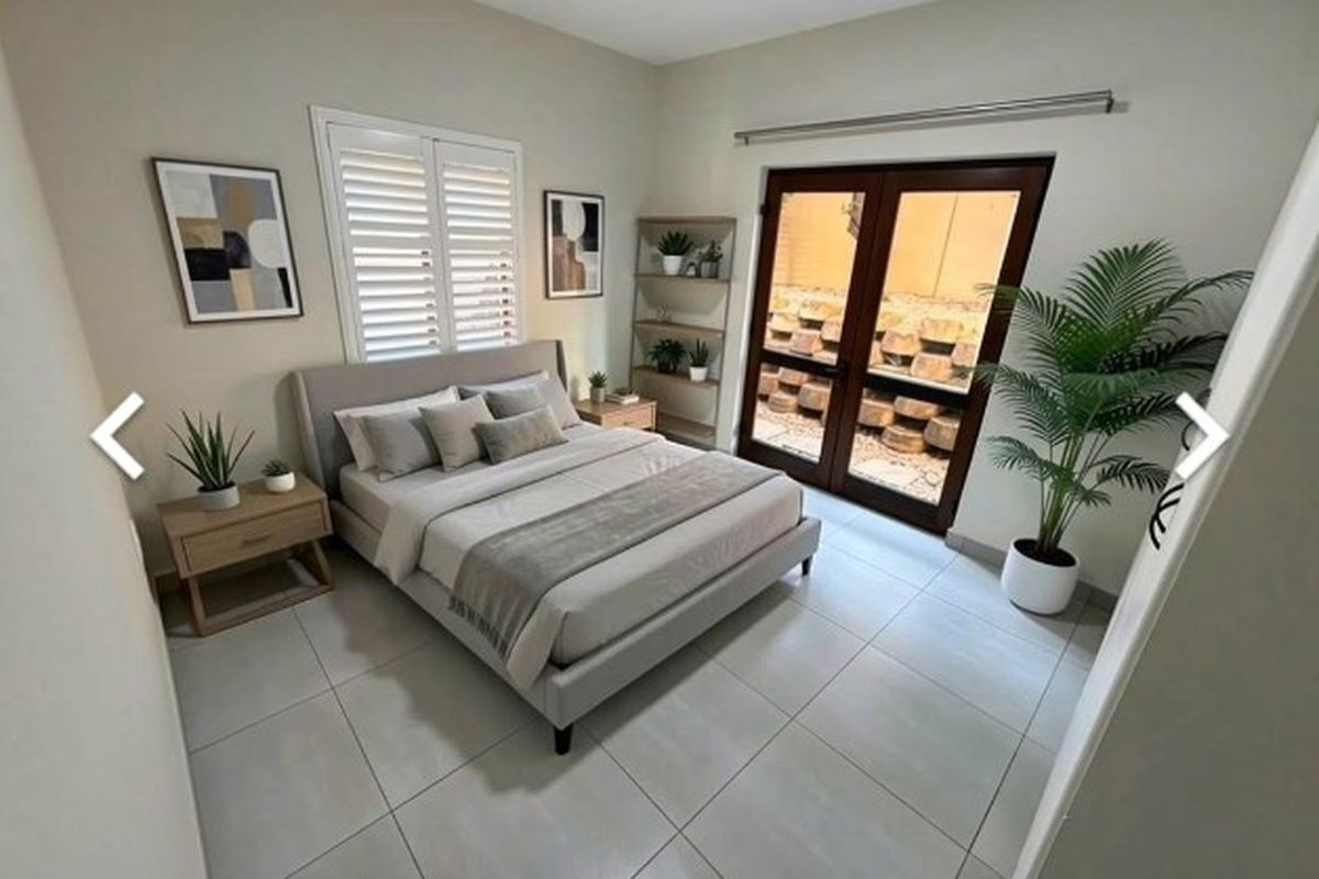 A well-maintained bedroom featuring neutral tiled flooring, plantation shutters, and double glass doors providing access to an outdoor area.