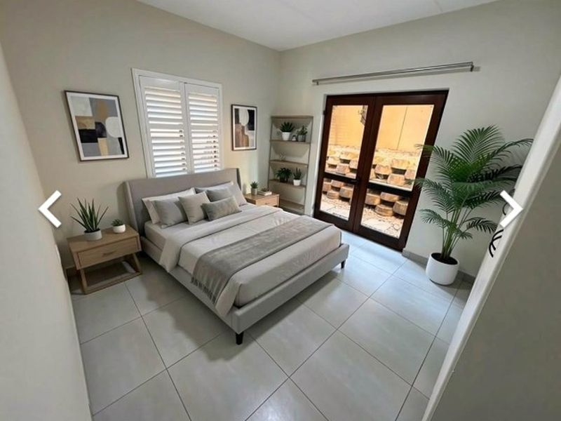 A well-maintained bedroom featuring neutral tiled flooring, plantation shutters, and double glass doors providing access to an outdoor area.