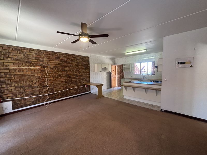 Open plan living and kitchen area featuring an exposed brick feature wall, ceiling fan, and breakfast bar, offering a blank canvas for renovation.