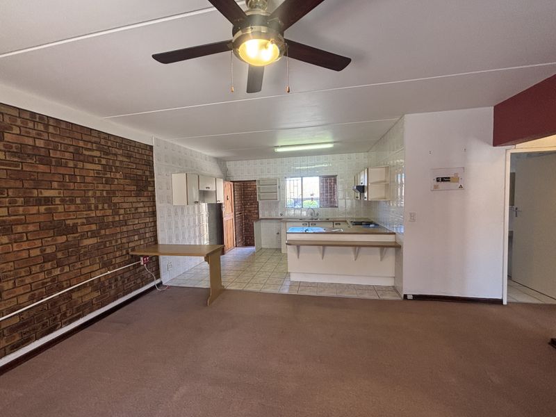 Open-plan living and kitchen area featuring an exposed brick wall, ceiling fan, and functional kitchen layout with breakfast bar, ready for modern updates.