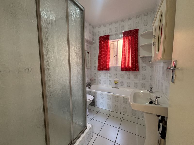 A dated bathroom featuring a shower enclosure, bathtub, pedestal basin, and toilet with original wall and floor tiling.