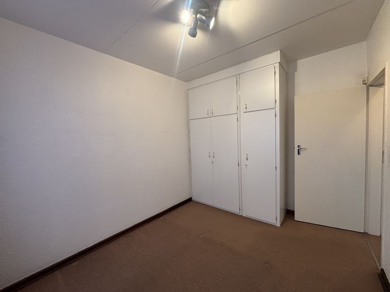 A vacant bedroom featuring built-in cupboards, carpeted flooring, and a standard ceiling light fixture, offering a blank canvas for personalization.