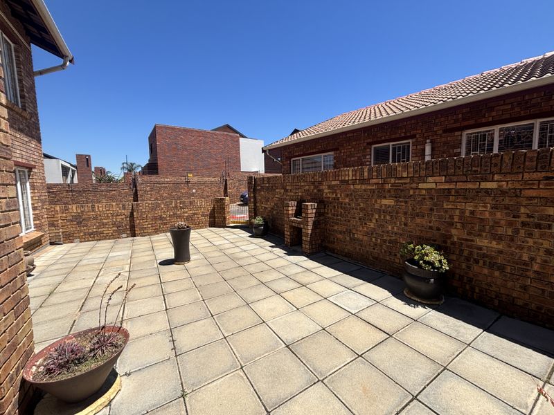 A private rear courtyard featuring paved flooring, a brick boundary wall, and a built-in brick braai area.