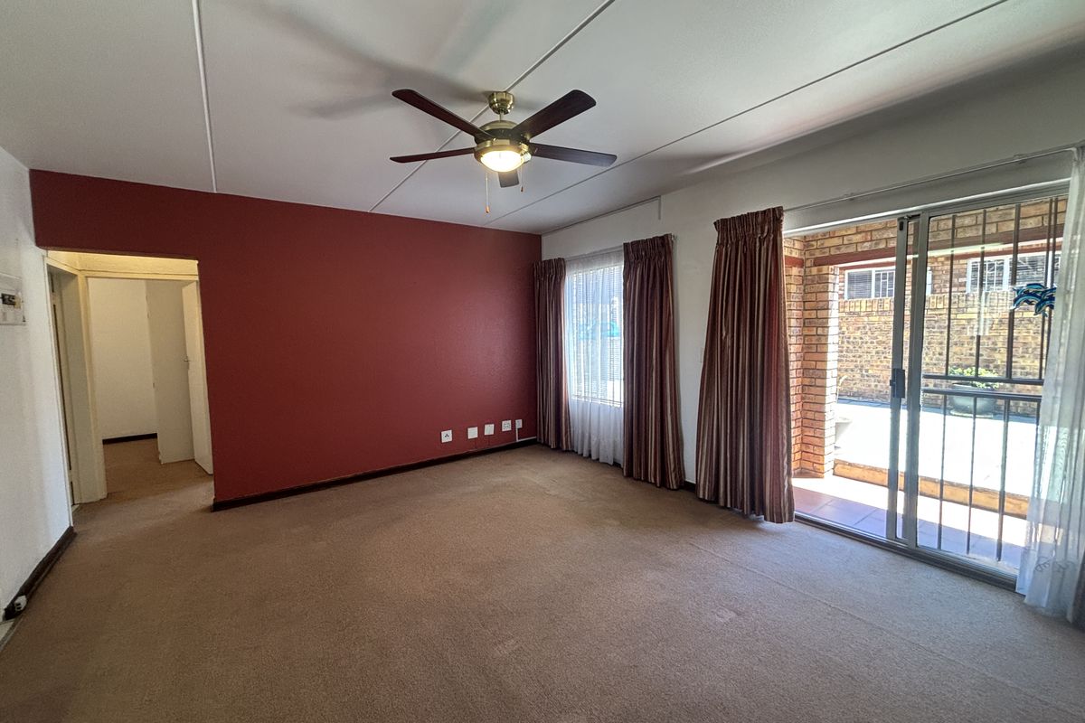 Spacious living room featuring a ceiling fan, carpeted flooring, and a sliding glass door providing access to the outdoor patio area.