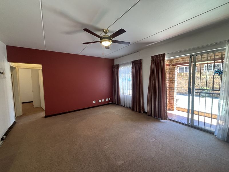 Spacious living room featuring a ceiling fan, carpeted flooring, and a sliding glass door providing access to the outdoor patio area.