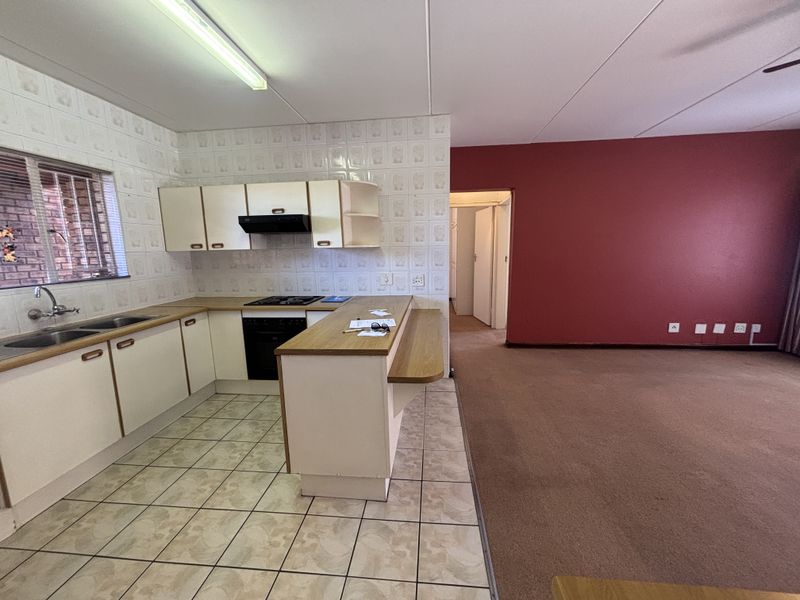Open-plan kitchen and living area featuring dated cabinetry, laminate countertops, and a combination of tiled and carpeted flooring in a spacious layout.