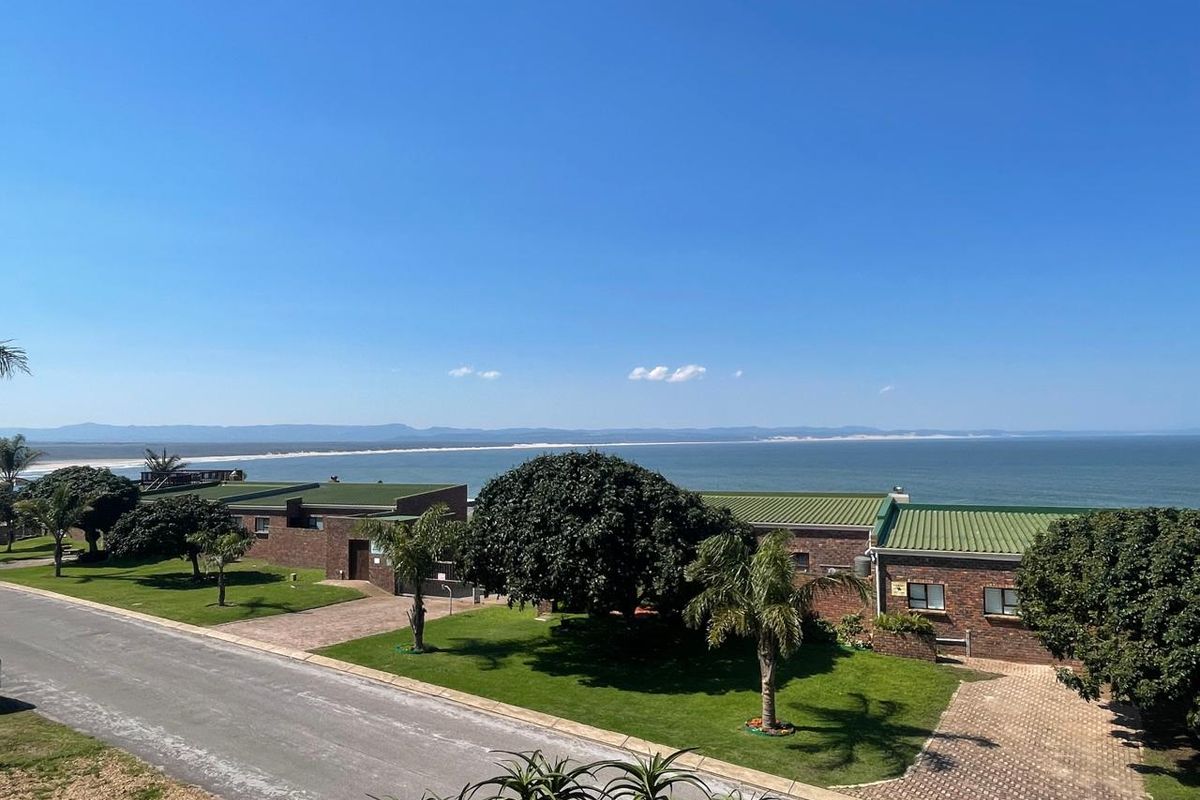 An elevated view of the townhouse complex featuring brick exteriors, green metal roofing, paved driveways, and well-maintained lawns overlooking the ocean.