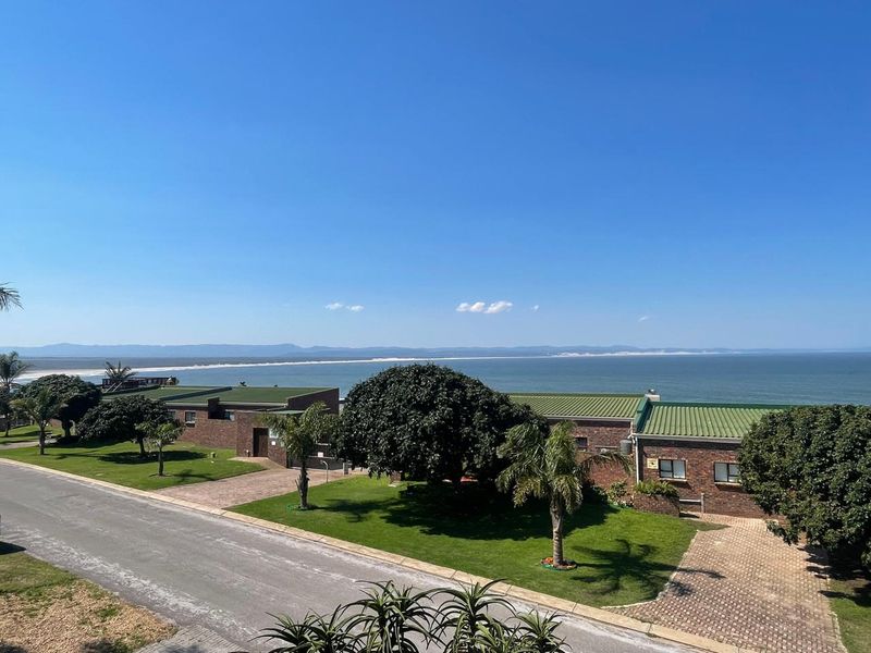 An elevated view of the townhouse complex featuring brick exteriors, green metal roofing, paved driveways, and well-maintained lawns overlooking the ocean.