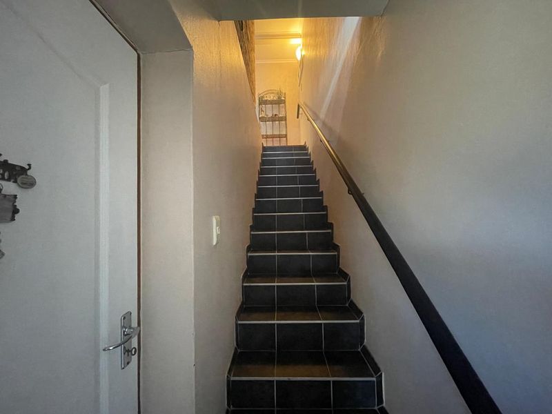 A functional staircase featuring dark tiled steps and a wall-mounted handrail, providing access between levels in the townhouse.