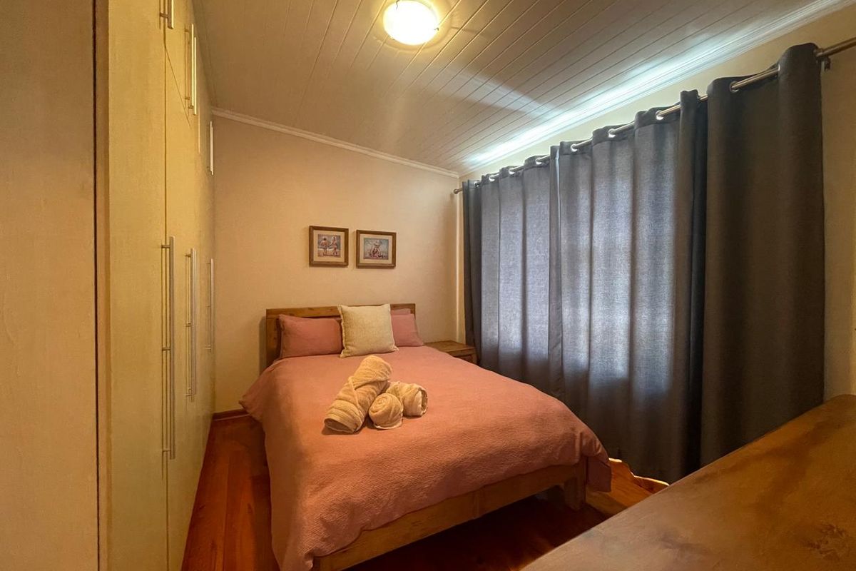 A cozy bedroom featuring warm timber flooring, a classic tongue and groove ceiling, and extensive built-in cupboard storage.