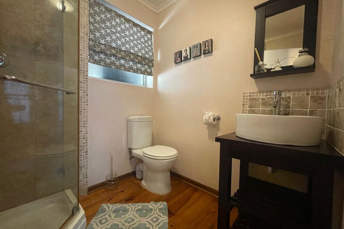 A functional bathroom featuring a glass-enclosed shower, a modern vessel sink on a vanity cabinet, and warm timber flooring.