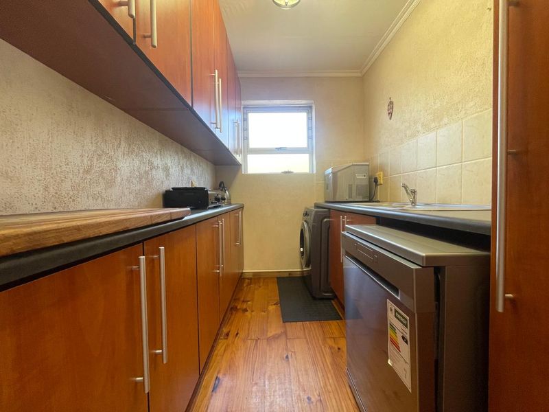 Functional scullery featuring timber flooring, ample built-in cabinetry, laminate countertops, and a stainless steel sink, providing efficient workspace for laundry and kitchen preparation.