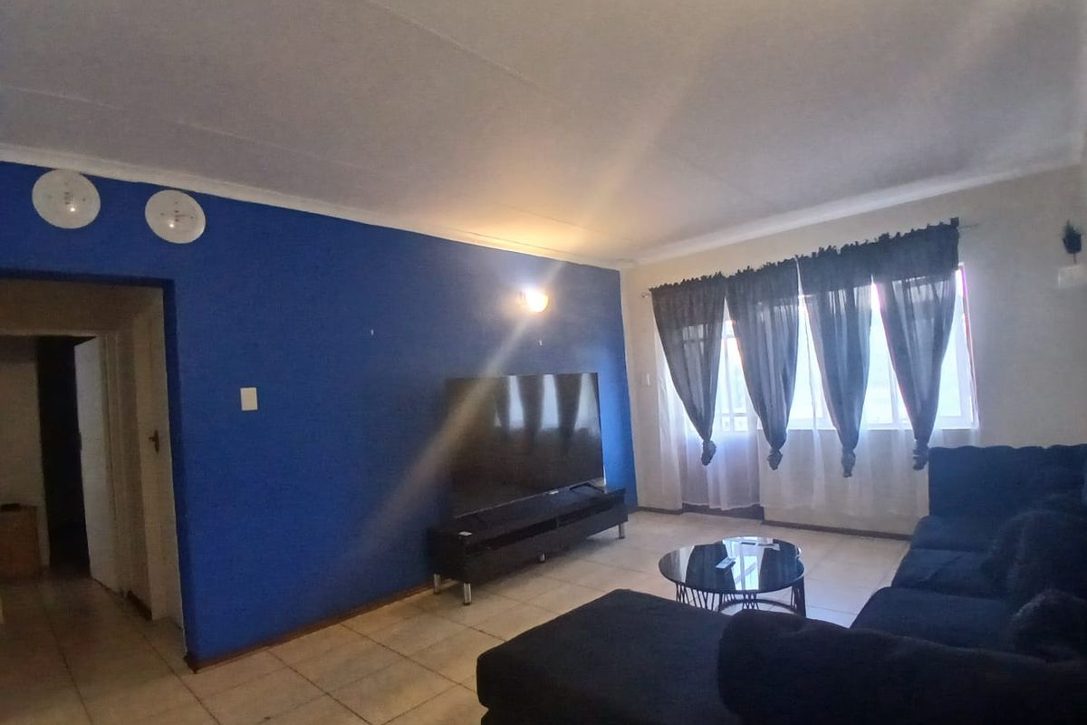 A living room featuring tiled flooring, a bold blue accent wall, and natural light from a large window.