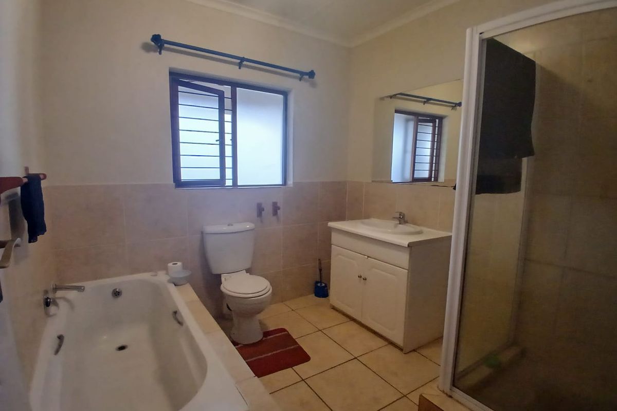 A functional bathroom featuring a bathtub, separate shower enclosure, built-in vanity, and tiled finishes throughout.
