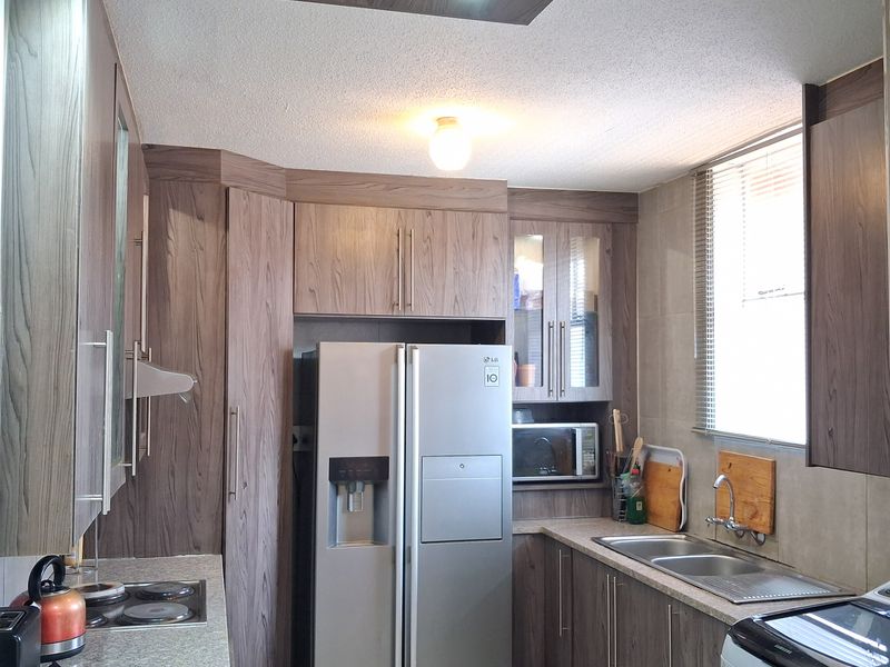 A functional kitchen featuring wood-grain cabinetry, a double sink, integrated hob with extractor, and built-in microwave, offering ample storage and workspace.
