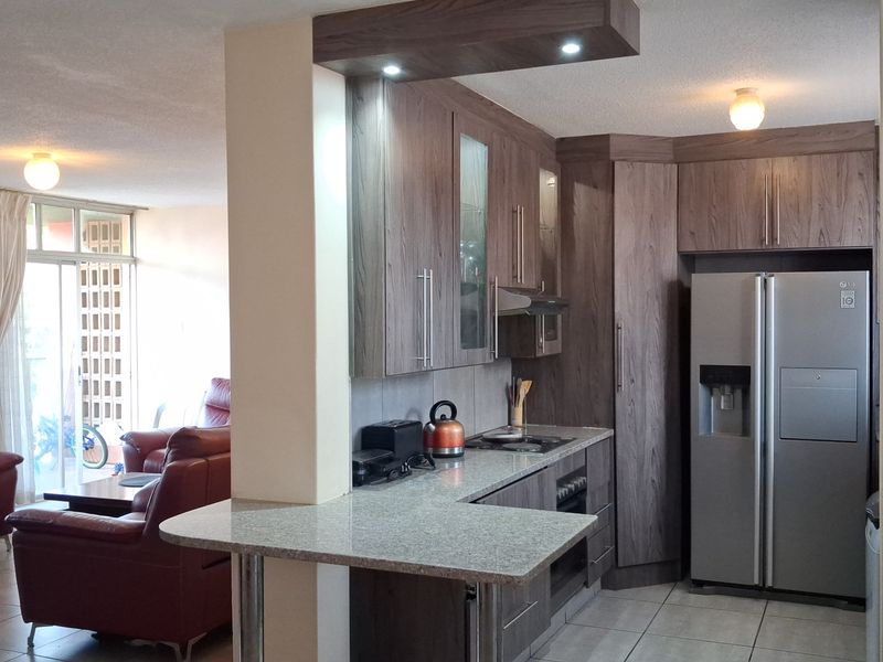 Open-plan kitchen featuring wood-finish cabinetry, granite countertops, a breakfast bar, and integrated appliances, seamlessly flowing into the adjacent living area.