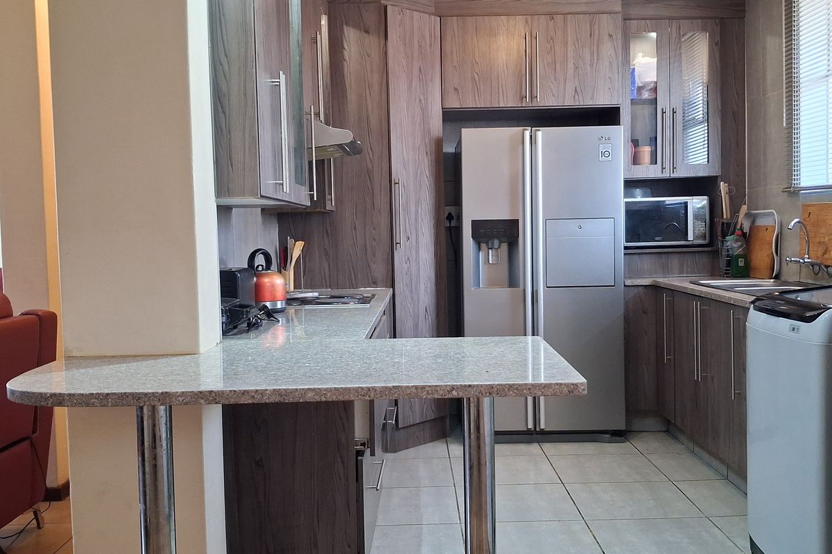 Functional kitchen featuring wood-look cabinetry, stone-effect countertops, a breakfast bar, and integrated appliances, offering a practical layout for daily meal preparation.