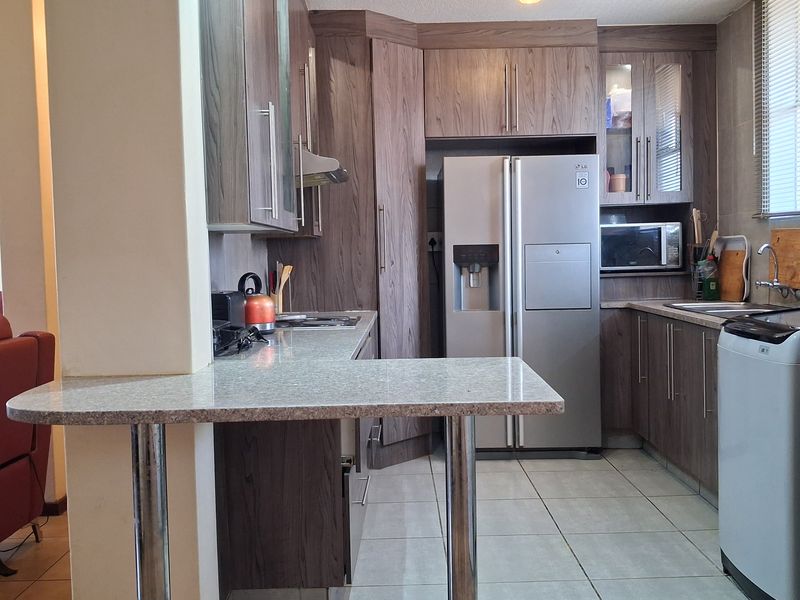 Functional kitchen featuring wood-look cabinetry, stone-effect countertops, a breakfast bar, and integrated appliances, offering a practical layout for daily meal preparation.