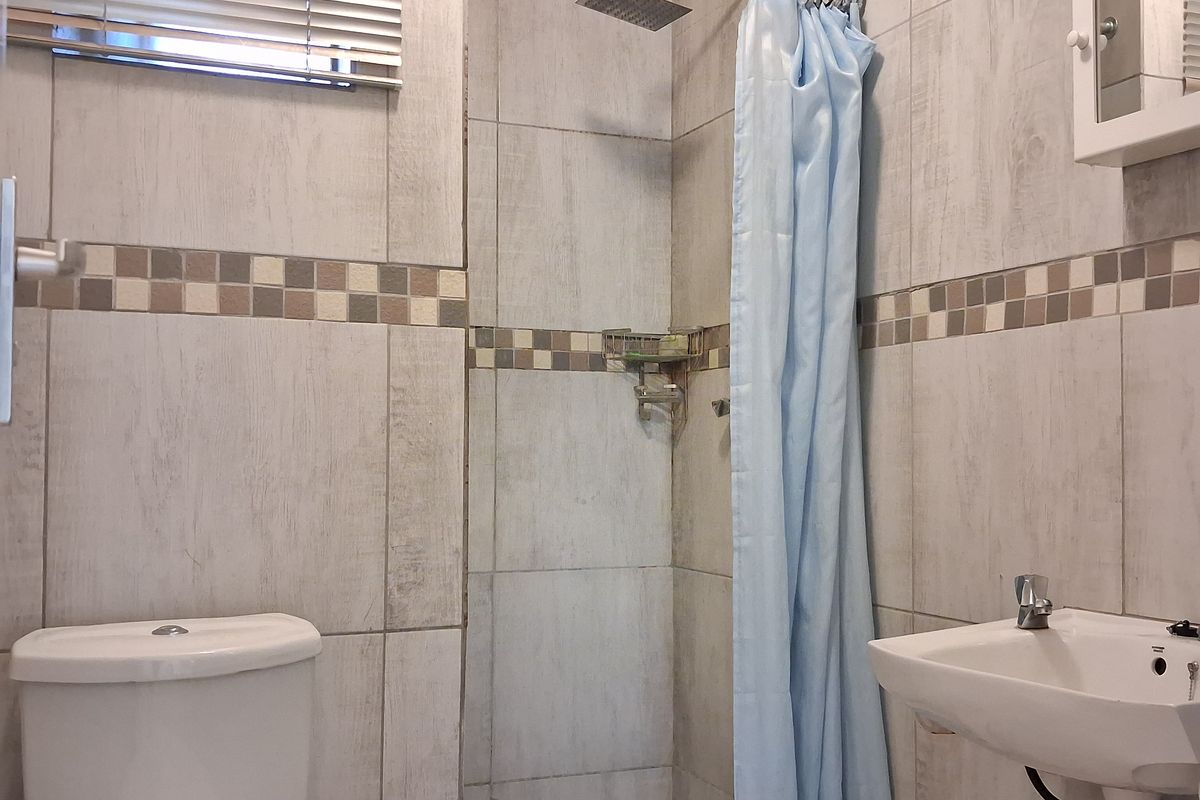A functional bathroom featuring a shower with a curtain, a wall-mounted basin, and a toilet, finished with neutral wall and floor tiling.
