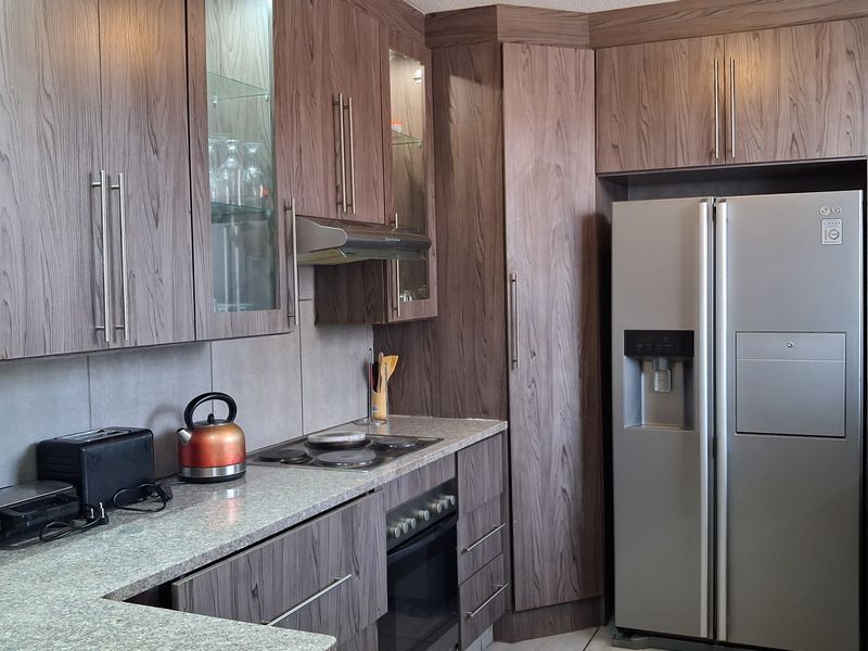 A functional kitchen featuring wood-grain cabinetry, stone countertops, integrated oven and hob, and tiled flooring, offering a practical and well-maintained cooking space.