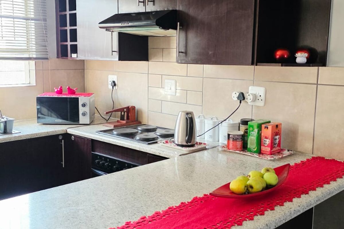 A functional kitchen featuring dark wood cabinetry, granite countertops, a tiled backsplash, and an integrated electric hob with an extractor fan.