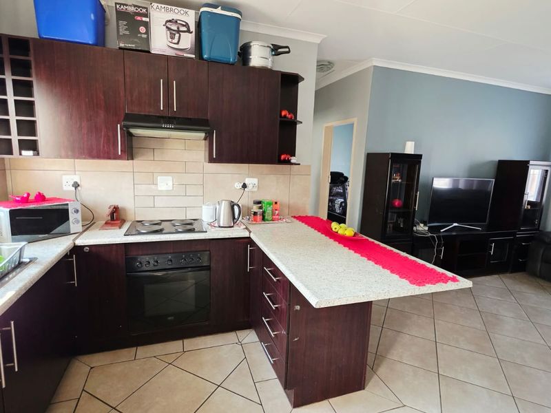 Open-plan kitchen and living area featuring dark wood cabinetry, built-in oven, electric hob, breakfast bar, and neutral ceramic floor tiles.