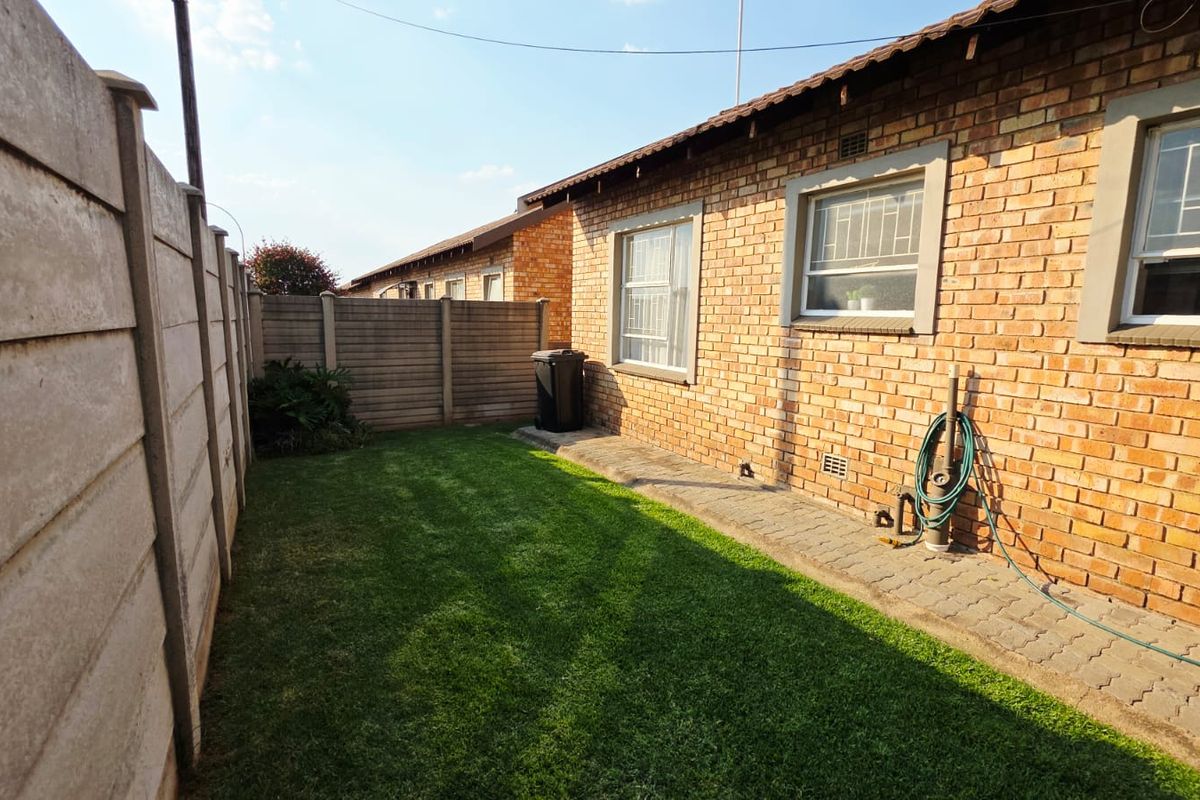 A private rear garden area featuring a well-maintained lawn, paved walkway, and brick townhouse exterior with secure window bars.