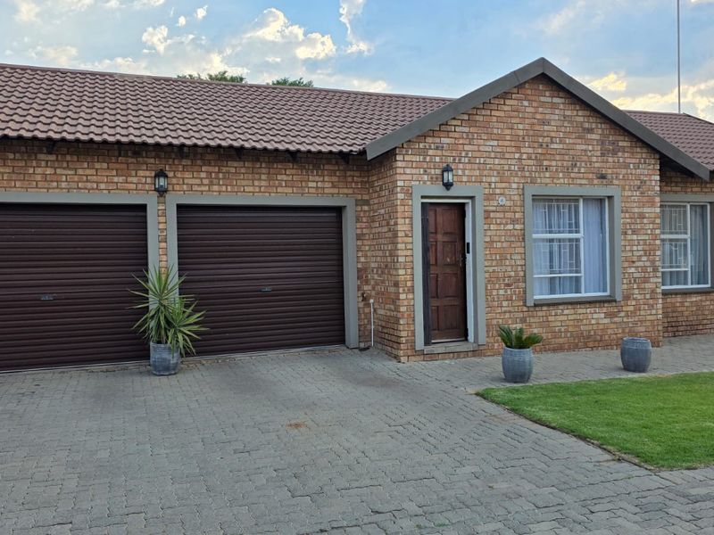 Front elevation of a townhouse featuring a double garage, face-brick exterior, tiled roof, and a paved driveway with a small front lawn.