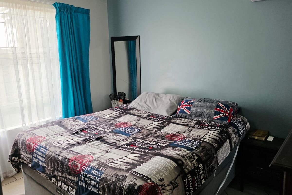 A functional bedroom featuring a window with security bars and a wall-mounted air conditioning unit.