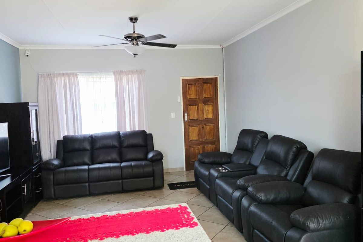 A spacious living room featuring tiled flooring, a ceiling fan, and a classic wooden door, offering a functional and comfortable living space.