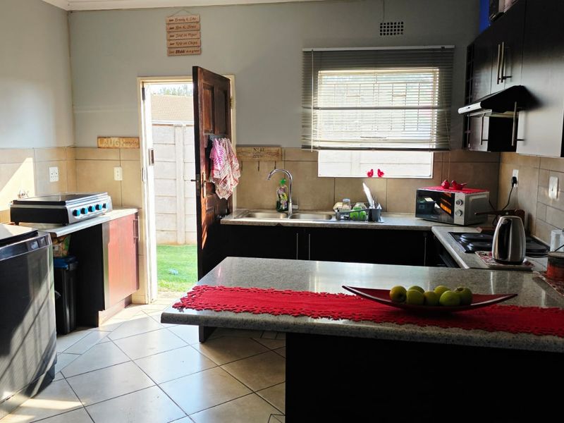 A functional kitchen featuring dark cabinetry, granite countertops, tiled backsplash, and direct access to the rear garden area.